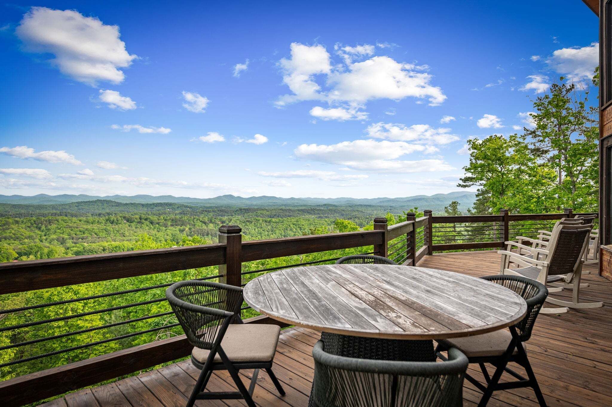 Une terrasse en bois avec une table ronde et des chaises, donnant sur un paysage boisé.