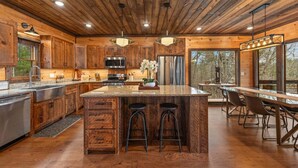 A rustic kitchen with wooden cabinets, a central island with stools, stainless steel appliances, and large windows. - 249 Ranger Station - Mountain View | Pet Friendly | Hot Tub | Shuffleboard | Cornhole (Morganton)