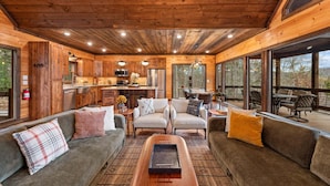 A wooden interior with a sofa, chairs, a coffee table, and a kitchen area. - 249 Ranger Station - Mountain View | Pet Friendly | Hot Tub | Shuffleboard | Cornhole (Morganton)