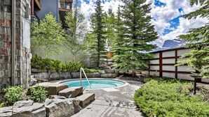 A backyard with a swimming pool, surrounded by stone steps and greenery. - Relaxing 1BR Getaway. Hot tub + Amazing Mtn Views (Canmore)