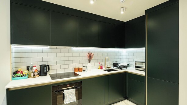 A modern kitchen with dark cabinets, a white countertop, and a tiled backsplash. - 2BR Garden Flat Near Richmond and Stadium (Twickenham)