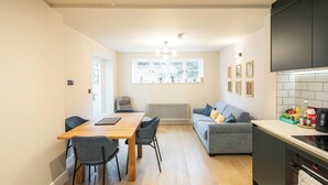 A modern kitchen with a dining area, a grey sofa, and a radiator. - 2BR Garden Flat Near Richmond and Stadium (Twickenham)