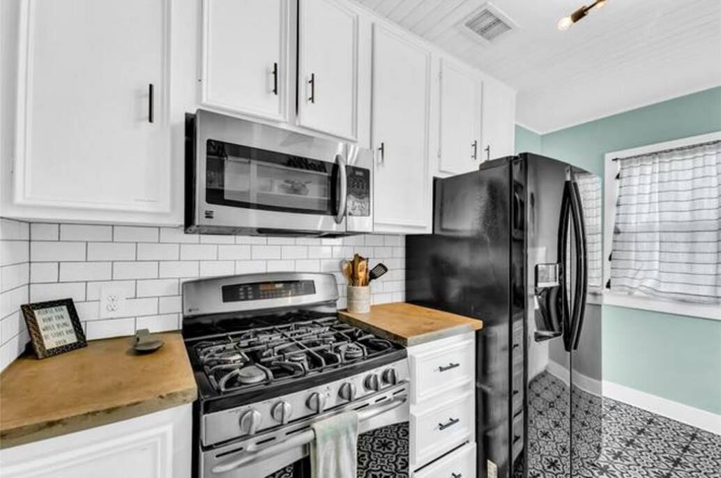 A kitchen with white cabinets, a black refrigerator, a microwave, and a stove.
