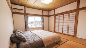 A traditional Japanese-style bedroom with tatami flooring, a futon bed, sliding shoji doors, and a view of the outside. - Luxe 6-bedroom Ski Lodge Myoko Kogen (Myoko)