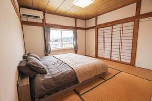 Un dormitorio de estilo japonés tradicional con suelo de tatami, futón, puertas correderas shoji y vistas al exterior.