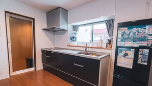 A modern kitchen with a built-in stove, a stainless steel range hood, and a black refrigerator with travel posters. - Luxe 6-bedroom Ski Lodge Myoko Kogen (Myoko)