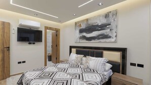 A modern bedroom with a geometric-patterned bedspread, a large abstract painting, and built-in lighting. - 2 BD Smart Luxury Apt in New Cairo (Cairo Governorate)