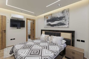 Ein modernes Schlafzimmer mit einem zudeckenden Bettlaken mit geometrischem Muster, einem großen abstrakten Gemälde und eingebauter Beleuchtung.