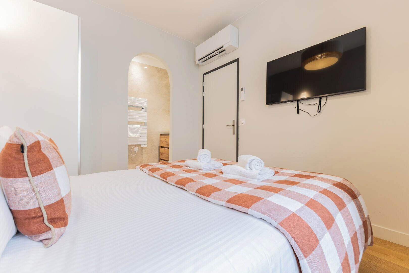 Et hotelværelse med en seng, et fjernsyn ophængt på væggen og en aircondition.