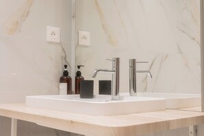 A bathroom with a white marble wall, a double sink with chrome faucets, and a mirror above the sink. - Luxury 3-bedroom apartment in hyper centre, air con, lift (Bordeaux)