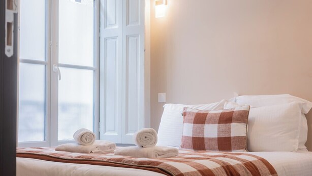 A hotel room with a bed, pillows, a checkered blanket, and rolled towels on the floor. - Luxury 3-bedroom apartment in hyper centre, air con, lift (Bordeaux)
