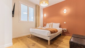 A bedroom with a bed, a nightstand, a lamp, a window with curtains, and a wooden floor. - Luxury 3-bedroom apartment in hyper centre, air con, lift (Bordeaux)