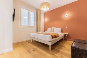 Ein Schlafzimmer mit einem Bett, einem Nachttisch, einer Lampe, einem Fenster mit Vorhängen und Holzboden.