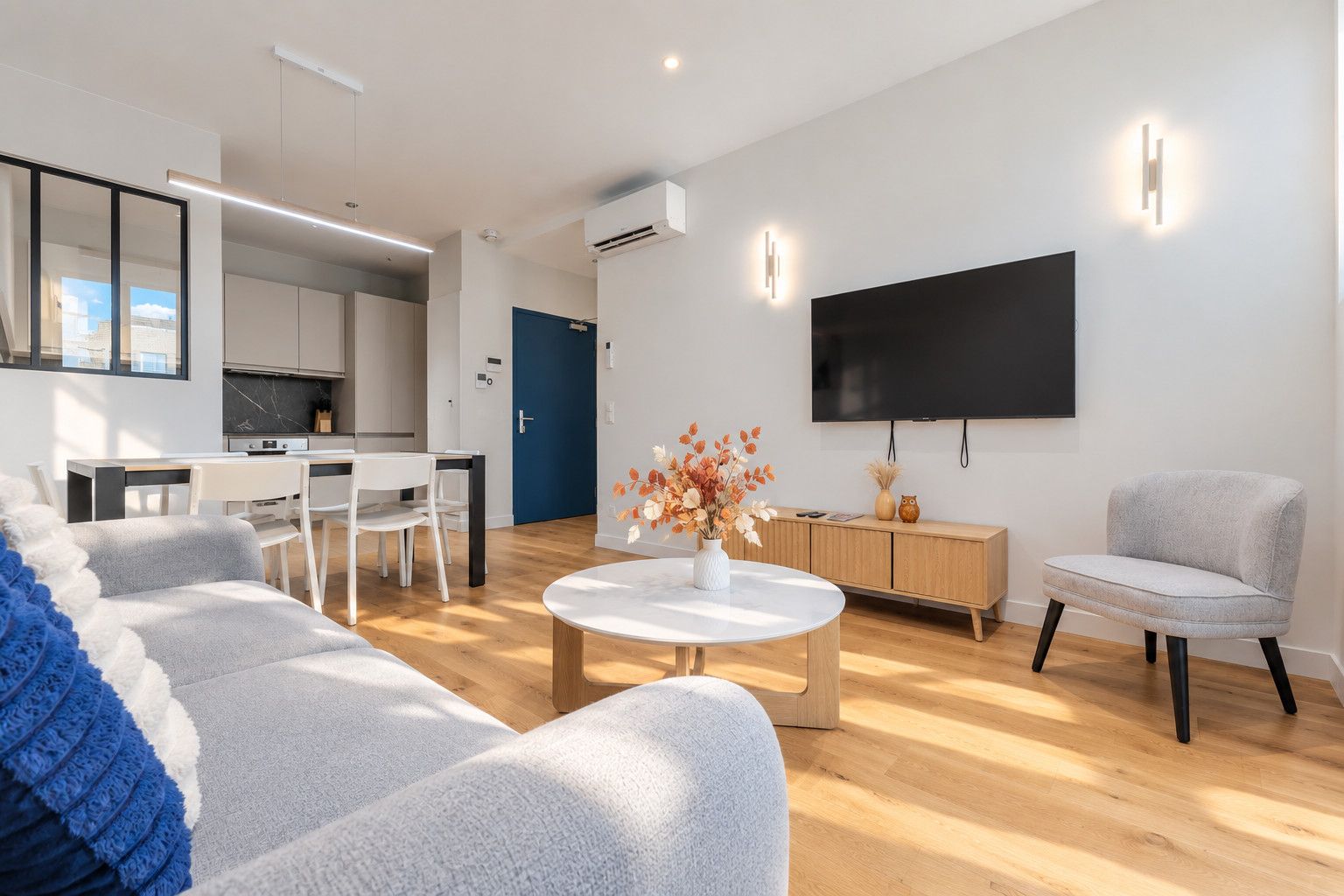 Un salon moderne comprenant un canapé, une table basse, un téléviseur et un coin repas avec des chaises et une table.