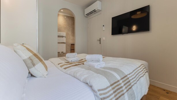 A hotel room with a bed, a TV mounted on the wall, and an air conditioning unit. - Luxury 3-bedroom apartment in hyper centre, air con, lift (Bordeaux)