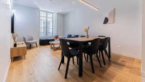 A modern dining area with a wooden table and black chairs, a sofa, and a window with a view. - Luxury 3-bedroom apartment in hyper centre, air con, lift (Bordeaux)