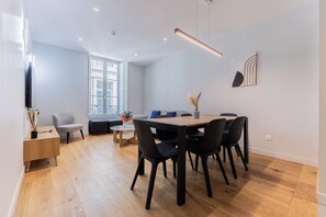 A modern dining area with a wooden table and black chairs, a sofa, and a window with a view. - Luxury 3-bedroom apartment in hyper centre, air con, lift (Bordeaux)