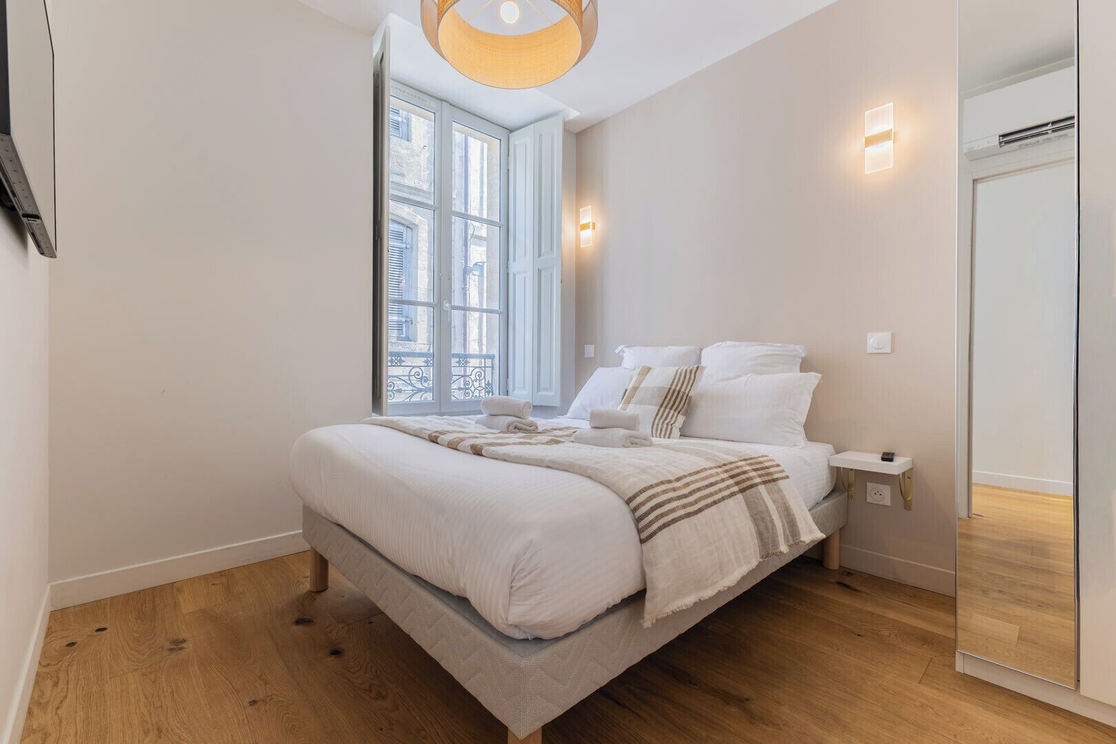A bedroom with a large bed, a bedside table, a nightstand, a window with a view, and a ceiling light fixture.