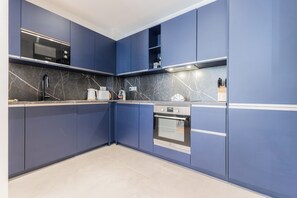 A modern kitchen with blue cabinets, a Bosch microwave, a built-in oven, and a marble backsplash. - Luxury 3-bedroom apartment in hyper centre, air con, lift (Bordeaux)