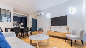 A modern living room with a flat-screen TV, a dining area, and a kitchen in the background. - Luxury 3-bedroom apartment in hyper centre, air con, lift (Bordeaux)