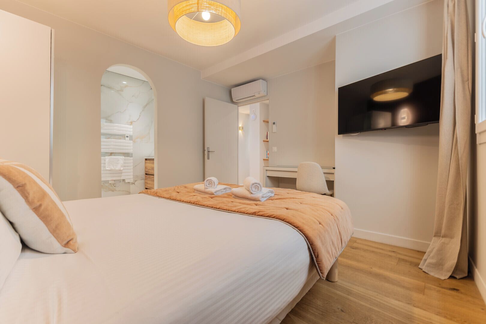 A hotel room with a bed, a desk, a chair, an air conditioning unit, and a television on the wall.
