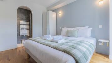 A hotel room with a bed, a wooden floor, a wall-mounted towel rack, and a light fixture.