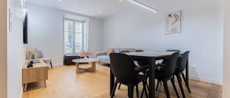 A modern dining area with a round table, black chairs, and a wooden floor.