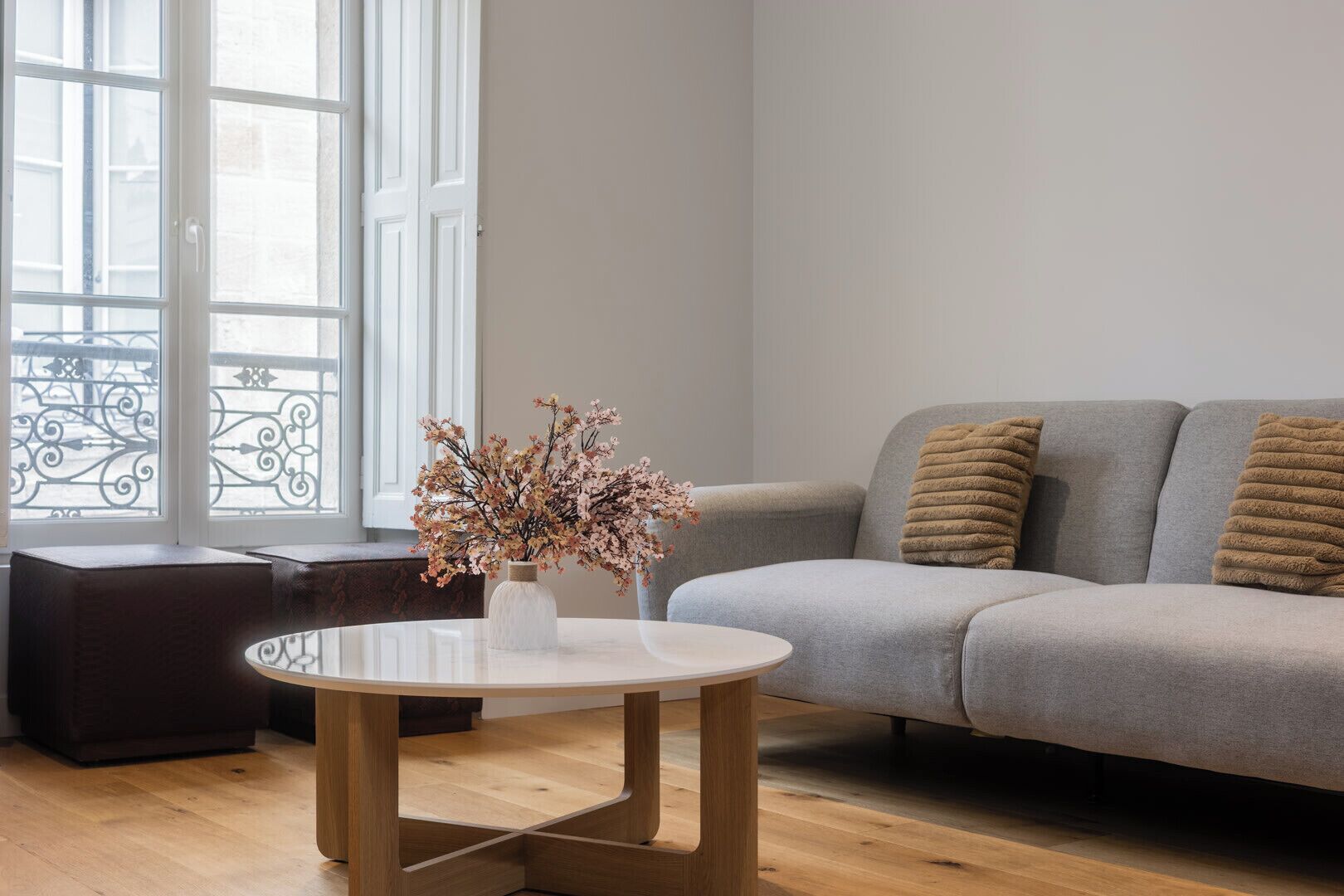 A modern living room with a grey sofa, a round wooden coffee table, and a vase with dried flowers.