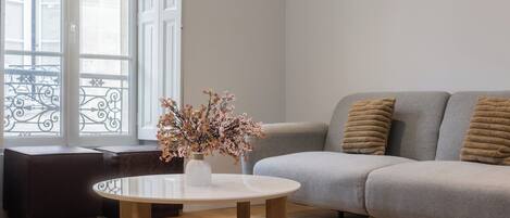 Un salón moderno con un sofá gris, una mesa de centro redonda de madera y un jarrón con flores secas.