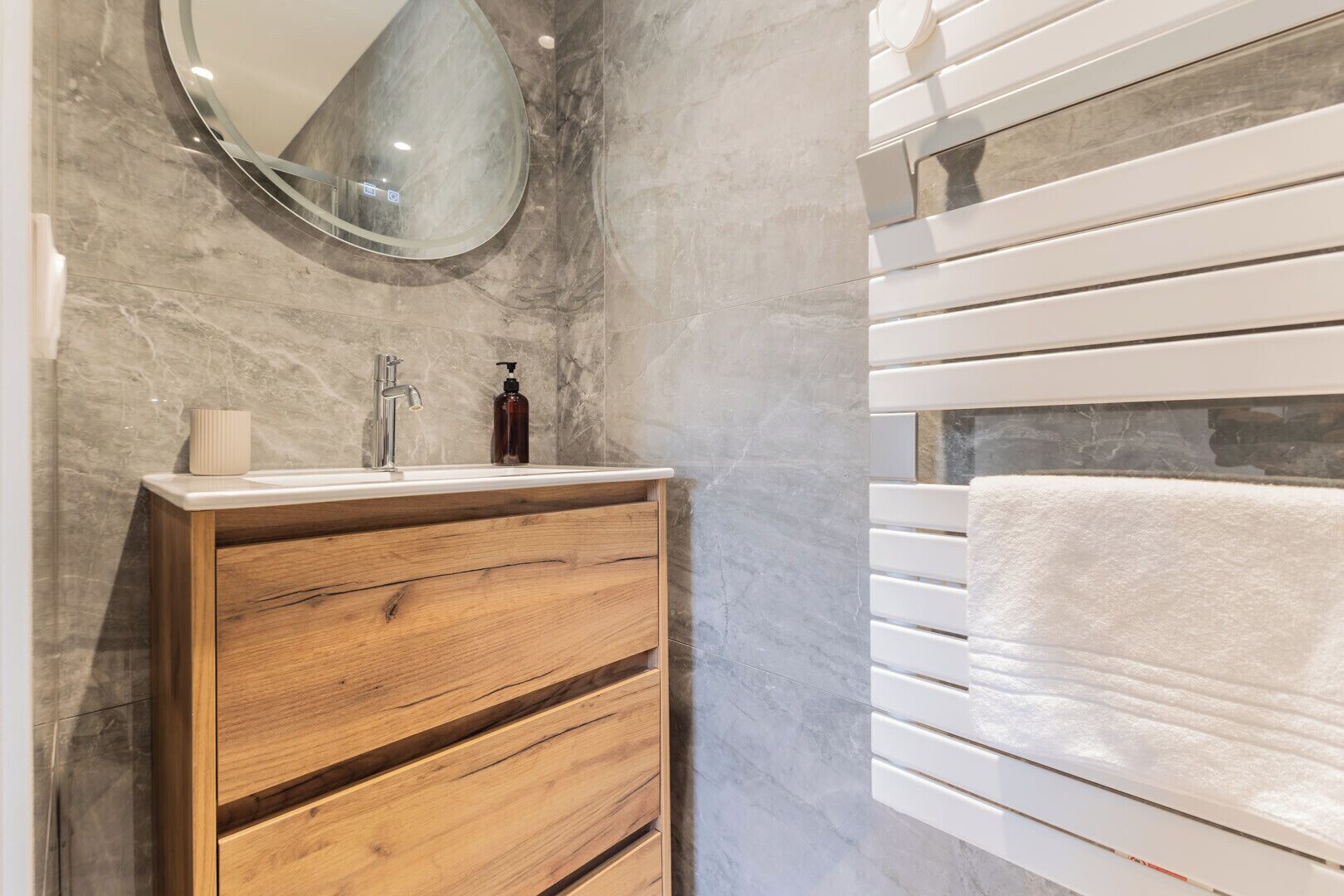 A bathroom with a wooden vanity, a mirror, a sink, and a towel rack.