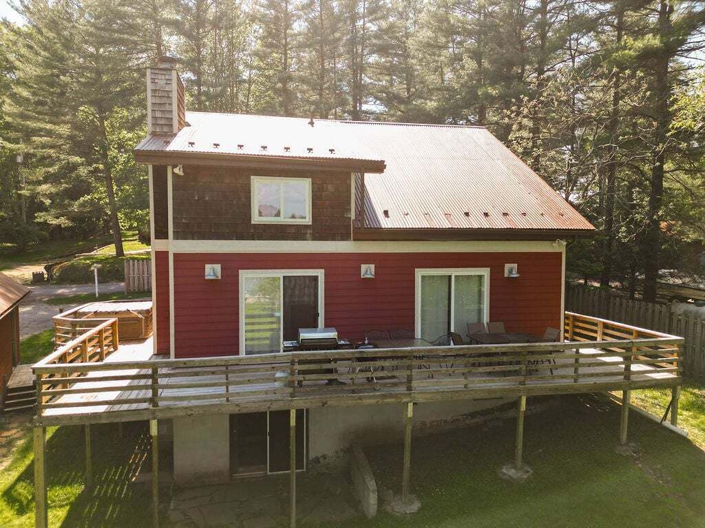 Une maison à deux étages avec une terrasse, une cheminée et une cour clôturée.