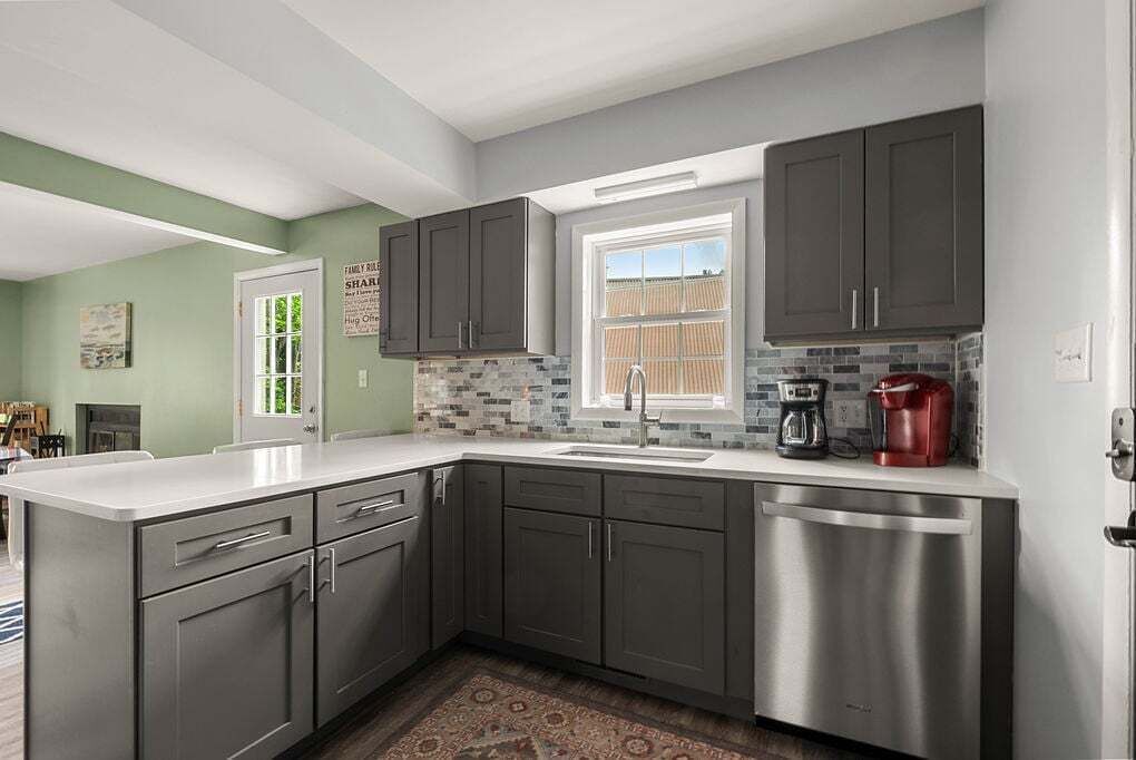 A modern kitchen with grey cabinets, a stainless steel dishwasher, and a tiled backsplash.