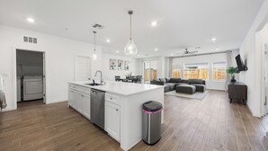 Cozinha moderna com ilha central, área de refeições com sofá e sala de estar com televisão.