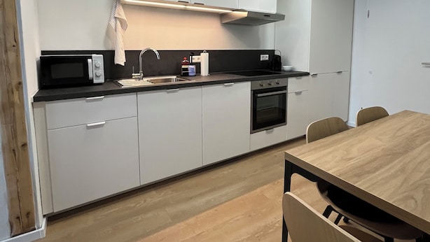 Une cuisine moderne avec des armoires blanches, un comptoir noir, un four encastré et une table à manger en bois avec des chaises.