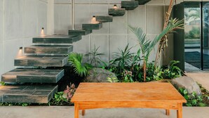 A staircase with wooden steps and a wooden handrail, surrounded by greenery and a concrete floor.