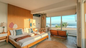 A modern bedroom with a large bed, wooden headboard, and a view of the ocean.