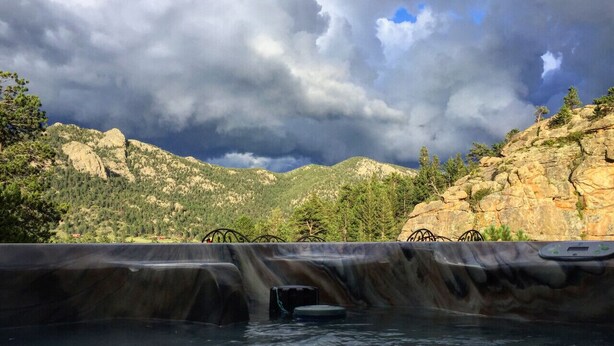 A hot tub with a waterfall feature, surrounded by rocky terrain and trees. - Hot tub, great views, huge deck. Near town, RMNP (Estes Park)