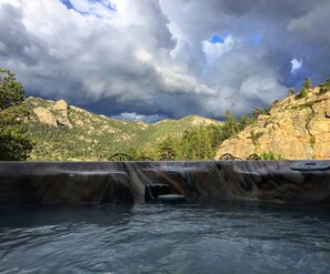 A hot tub with a waterfall feature, surrounded by rocky terrain and trees. - Hot tub, great views, huge deck. Near town, RMNP (Estes Park)