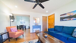 Ein Wohnzimmer mit blauem Sofa, orangefarbenem Sessel, Holztisch und einem gemusterten Teppich.