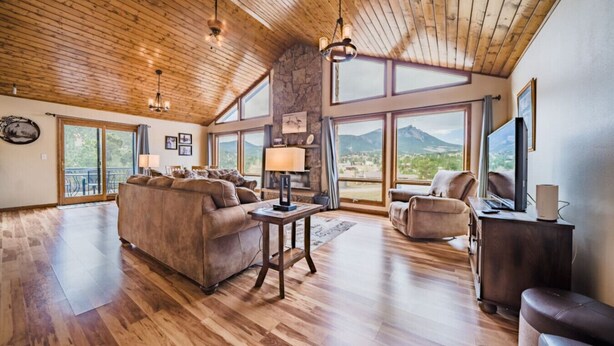 Ein geräumiges Wohnzimmer mit hohen Decken, Holzböden und großen Fenstern mit Blick auf die Berge.