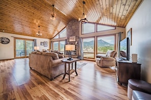 A spacious living room with a high ceiling, wooden flooring, and large windows offering mountain views. - Mtn view King beds all b-rooms near town qt area (Estes Park)