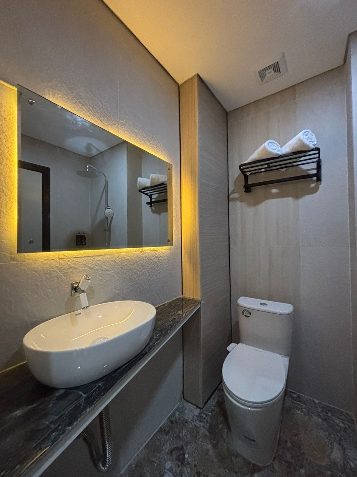 Un bagno moderno con uno specchio grande, un lavandino bianco, un water e un porta asciugamani.