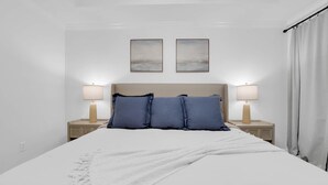 A neatly made bed with a white duvet and blue pillows, two bedside lamps, and a wall-mounted picture frame. - Cozy 3BR Home in Montgomery (Montgomery)
