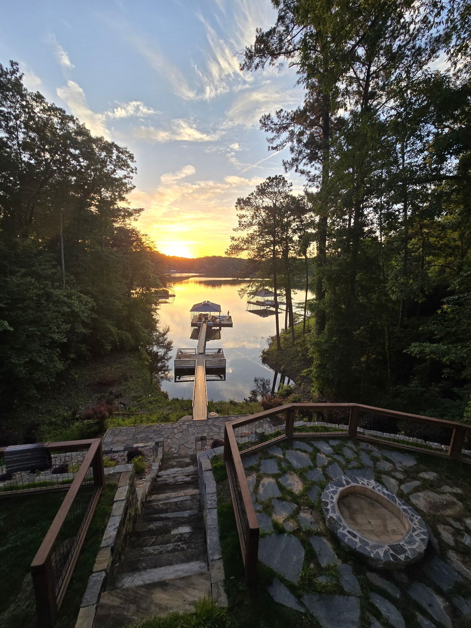 Una escalera de madera conduce a un mirador sobre un lago, rodeado de árboles y escalones de piedra.