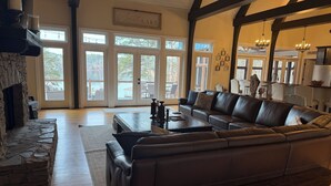 A spacious living room with a stone fireplace, leather sofa, and large windows offering views of the outdoors. - Enjoy beautiful sunsets at Blue Bird Cove on Lewis Smith Lake with private dock. (Crane Hill)
