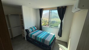 Ein Schlafzimmer mit Bett, Kleiderschrank, einem Fenster mit Vorhängen und einer Klimaanlage.
