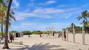 Uma praia com palmeiras, uma rede de voleibol e uma torre de salva-vidas.