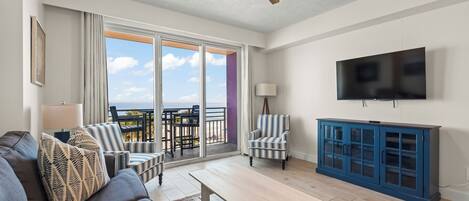 Un salon comprenant un canapé, des fauteuils, une table basse, un téléviseur et un balcon avec vue.