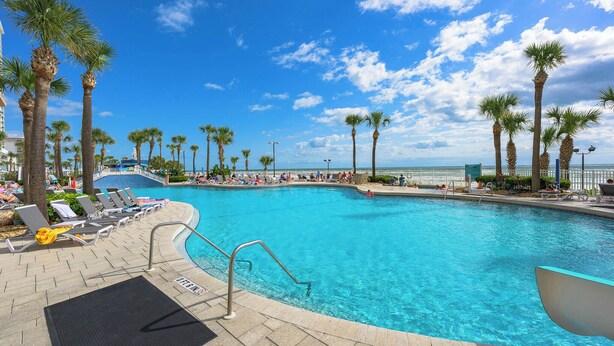 A pool area with palm trees, lounge chairs, and a clear view of the ocean. - Palm Royale - Ocean Walk (Daytona Beach)