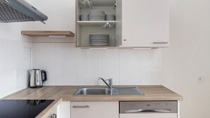 A modern kitchen with a built-in dishwasher, a sink, and a cabinet with stacked plates. - Blueground | Innere Stadt, view, nr Danube Canal (Vienna)